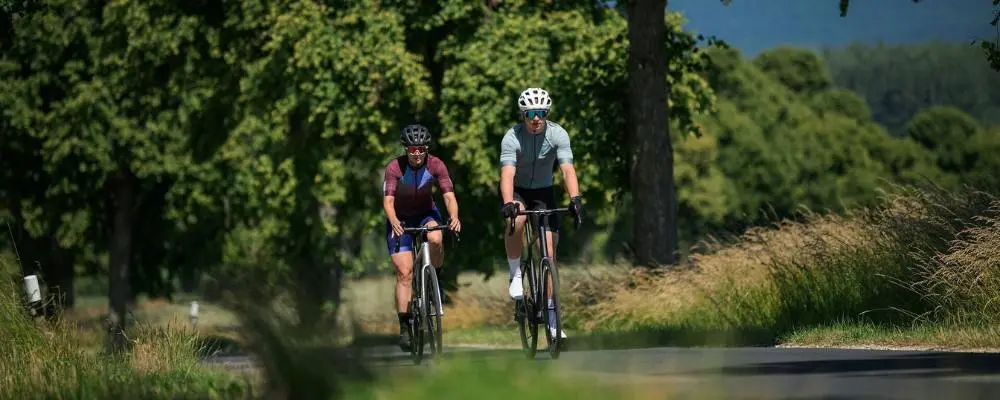 Deux cyclistes roulant sur une route de campagne bordée d’arbres, sortie vélo de route